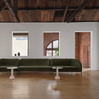Green velvet sofa with light gray tabletops, warm wood floors, and exposed brick walls. Modern, earthy color palette.