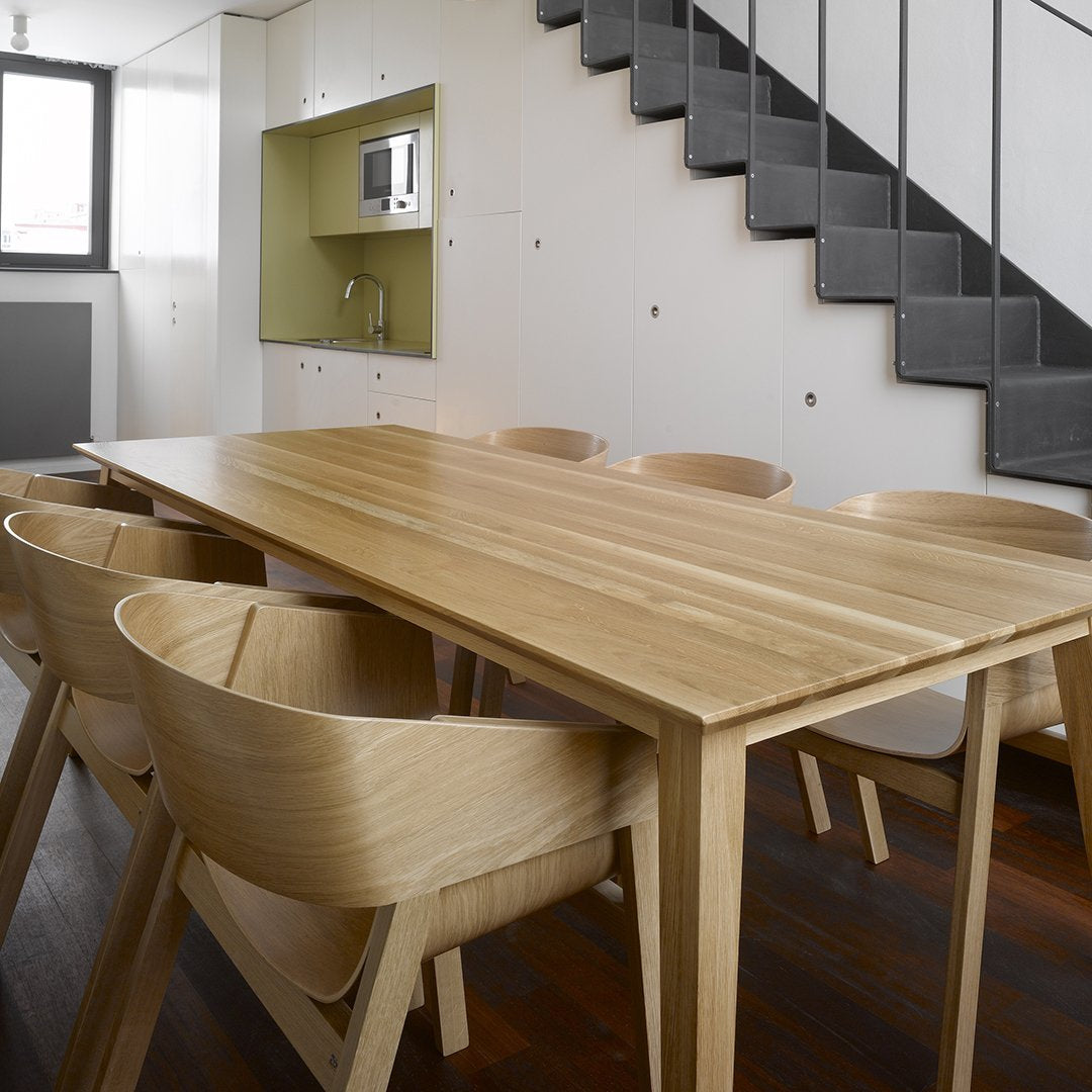 Light wooden dining table with smooth finish, paired with round, natural wood chairs in a modern setting.