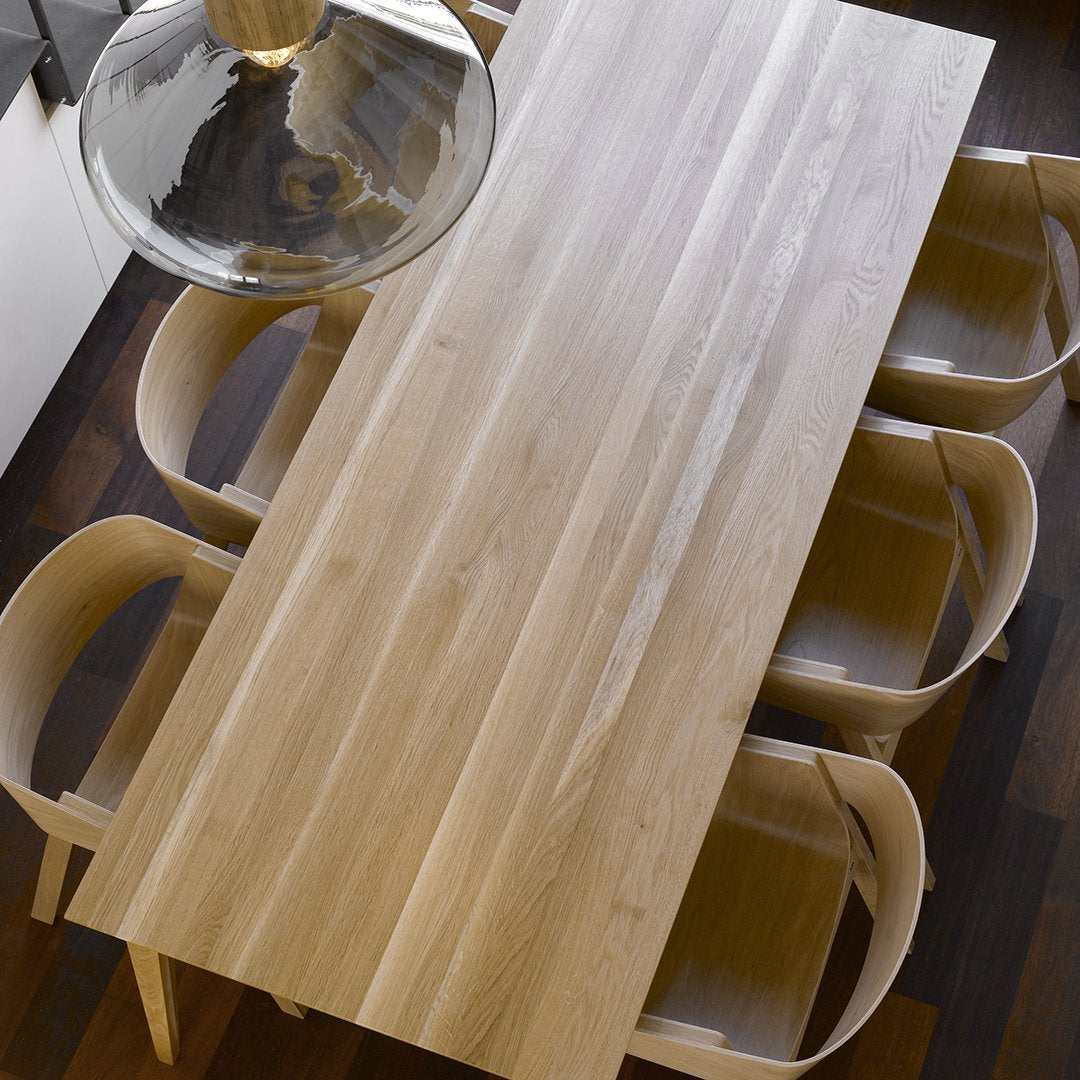 Natural wood dining table with light beige tones and smooth grain pattern, complemented by matching curved chairs.