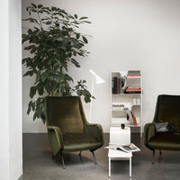 Green velvet armchairs with mid-century design, paired with a sleek white side table against a neutral backdrop.