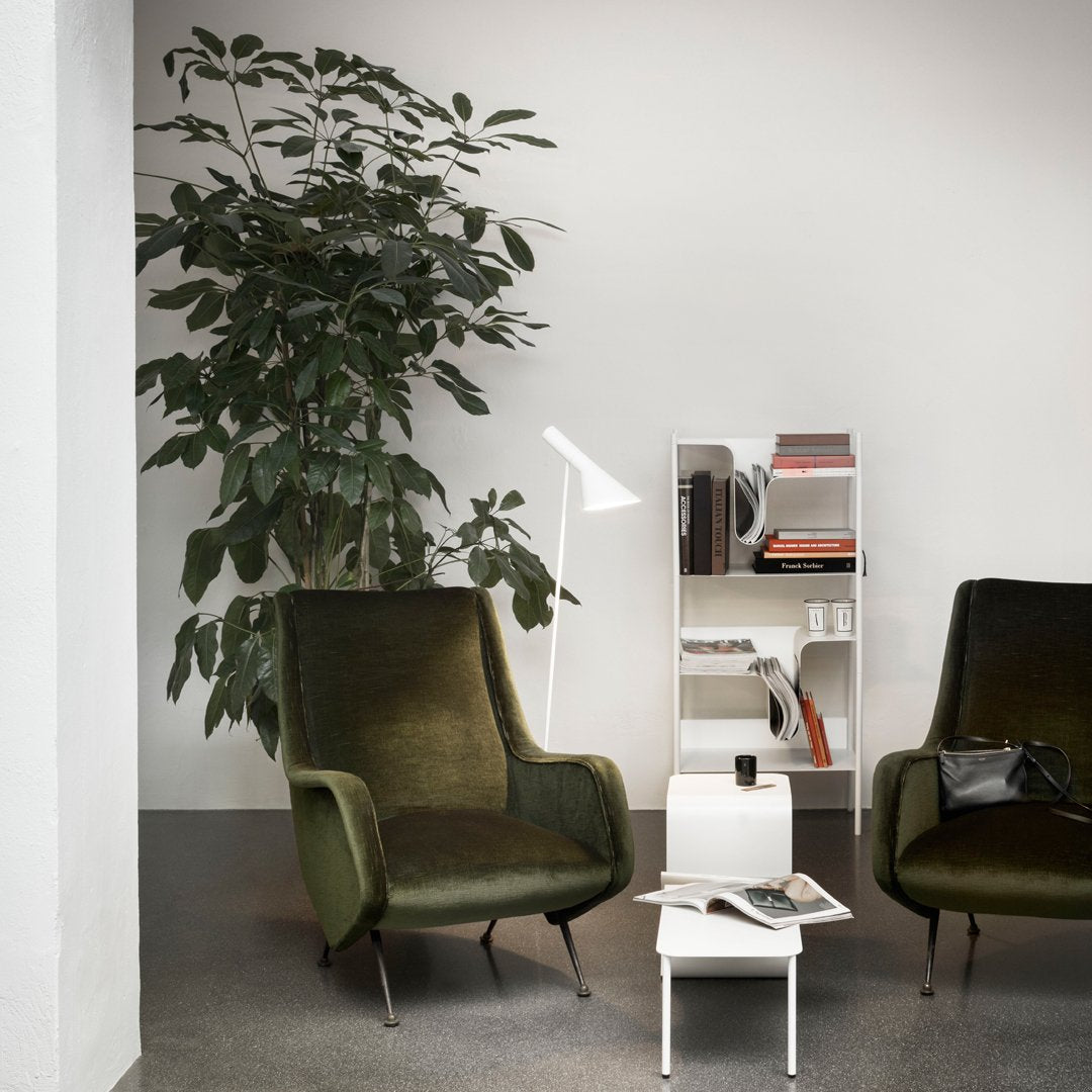 "Pair of olive green velvet chairs with minimalist white table and bookshelf, set against a neutral background."