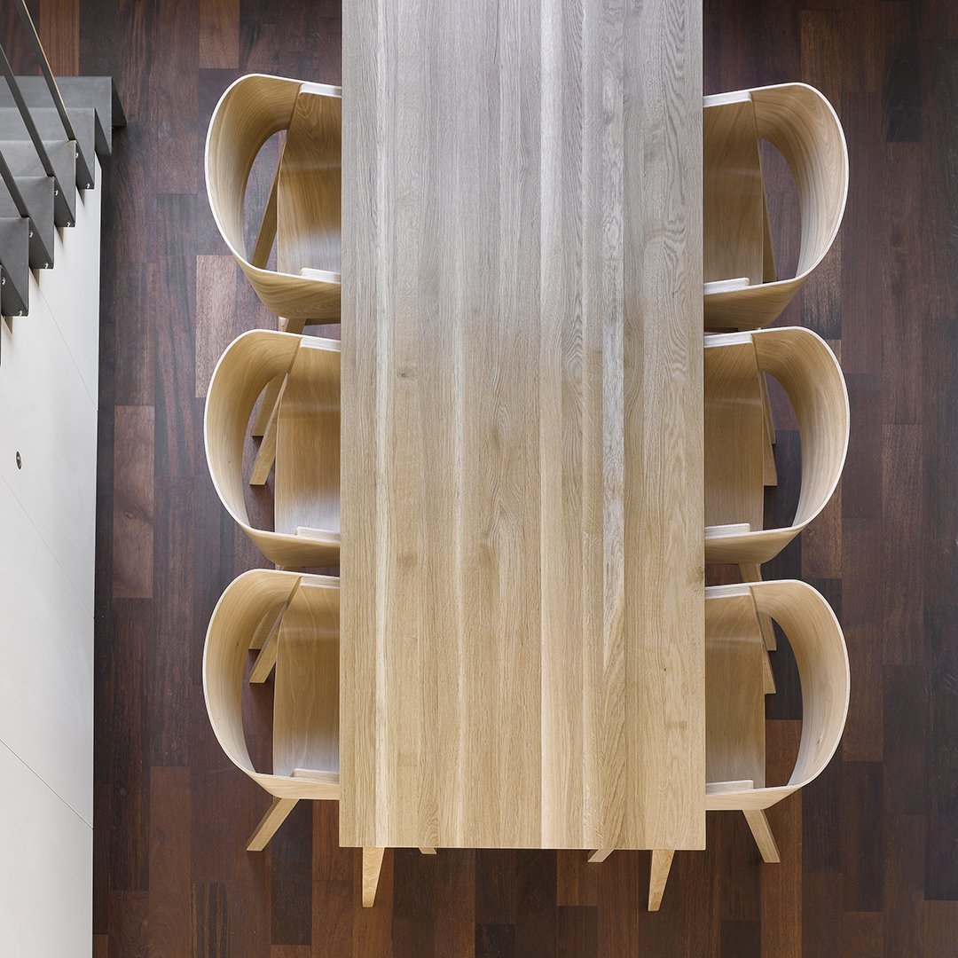 Light wood dining table with a smooth finish and four stylish, curved white chairs on a dark wooden floor.