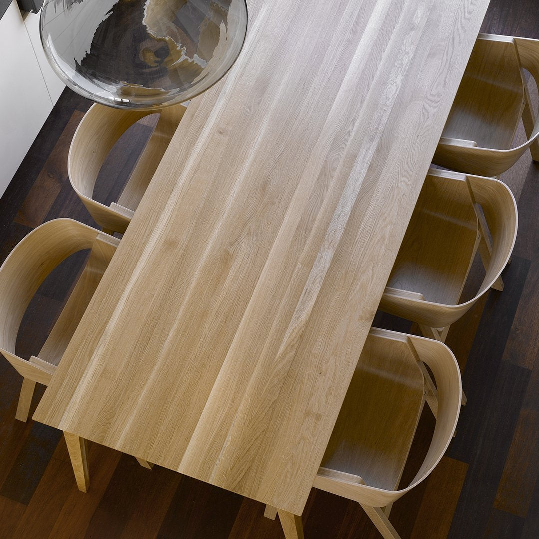 Light oak dining table with smooth grain pattern and minimalist design, accented by warm wooden chairs.