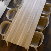 Light oak dining table with smooth grain pattern and minimalist design, accented by warm wooden chairs.