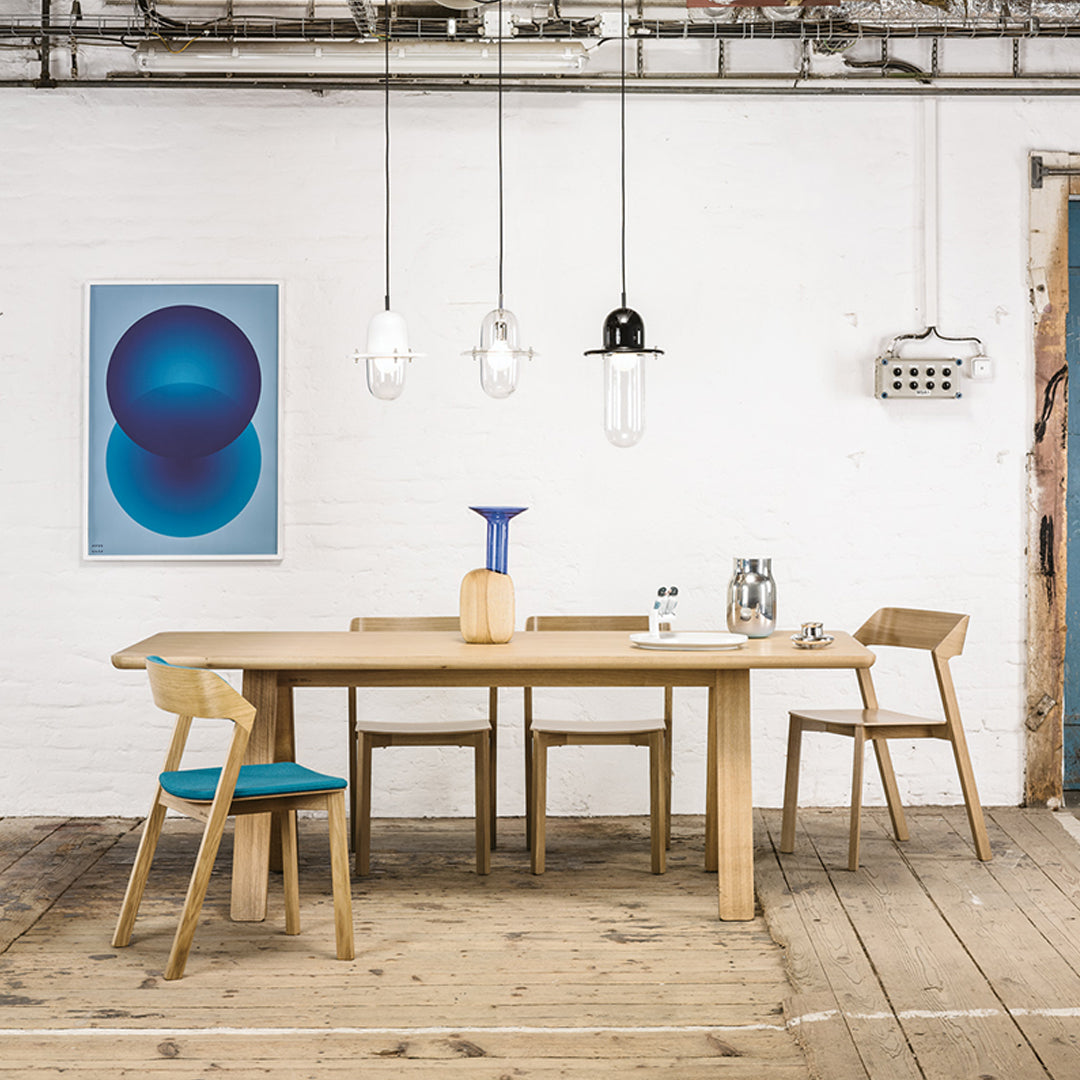 Scandinavian dining table with natural wood finish, teal chair cushions, and vibrant blue wall art. Minimalist decor style.