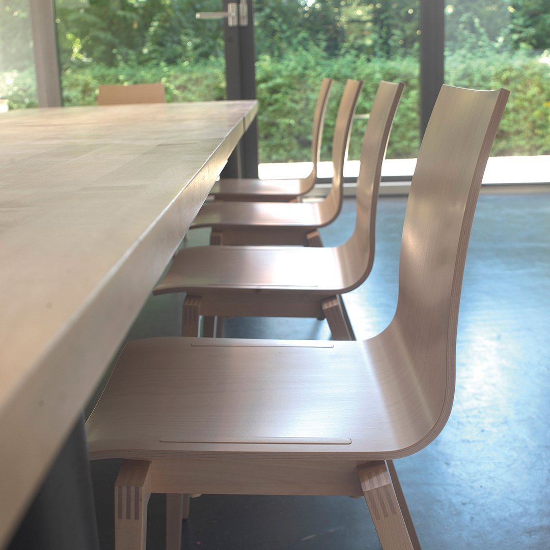 Light wood dining chairs with smooth finishes, arranged neatly beside a modern table in a spacious, bright setting.