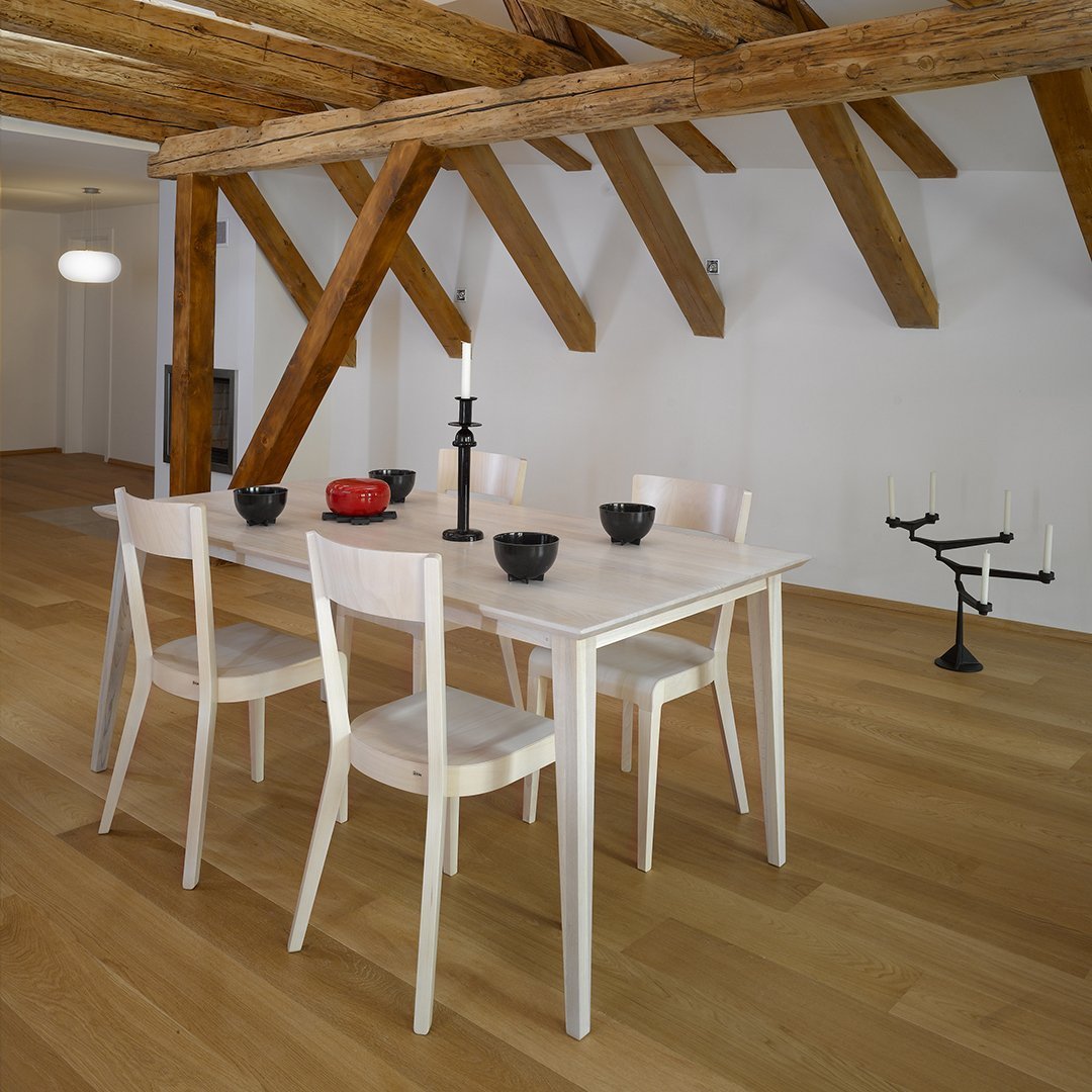 Stylish white dining table with four matching chairs, set against warm wooden beams and a light hardwood floor.