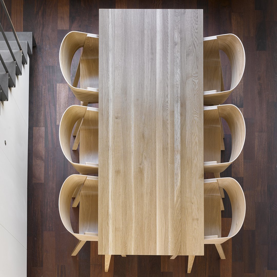 Light wooden table with a smooth finish, complemented by soft beige chairs against a rich dark wood floor.