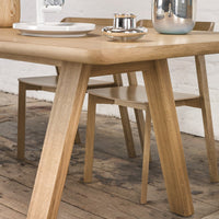 Natural oak dining table with smooth surfaces and minimalistic design, complemented by neutral-toned chairs and decor.
