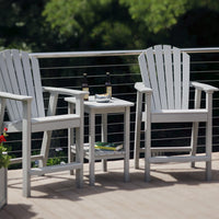 "White Adirondack chairs with a matching side table, set against a green outdoor backdrop."