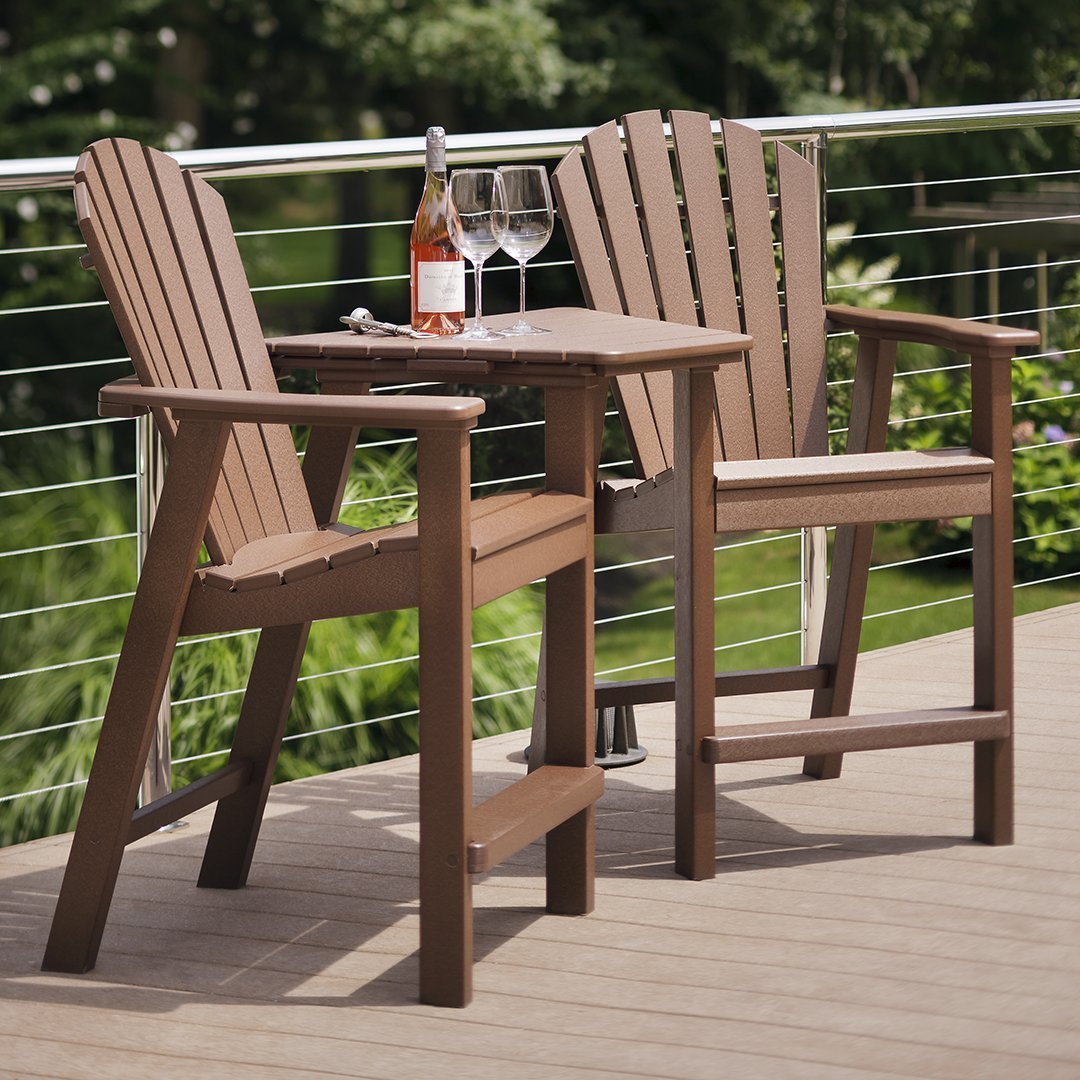"Brown adirondack chairs with slatted design and a matching table, set on a deck surrounded by greenery."