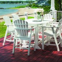White outdoor furniture set on a red deck, with green grass and a beach view in the background.