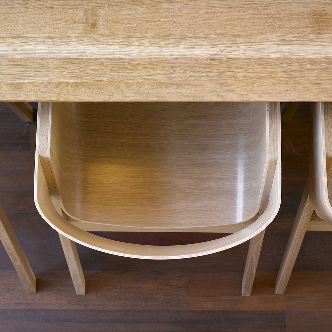 Light oak dining table with smooth finish; natural wood grains and round, minimalist chair design in neutral tones.