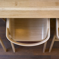 Light oak dining table with smooth finish; natural wood grains and round, minimalist chair design in neutral tones.