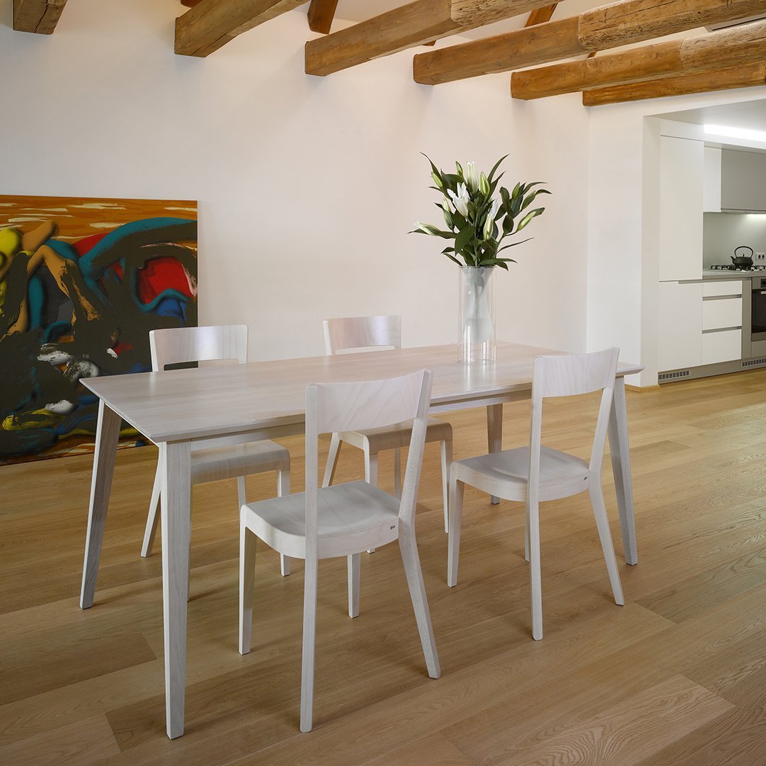 White dining table with minimalist design, complemented by light wood flooring and colorful abstract wall art.