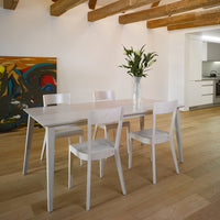 White dining table with minimalist design, complemented by light wood flooring and colorful abstract wall art.