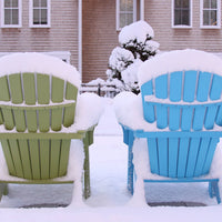 Green and blue Adirondack chairs partially covered in snow, set against a winter backdrop.
