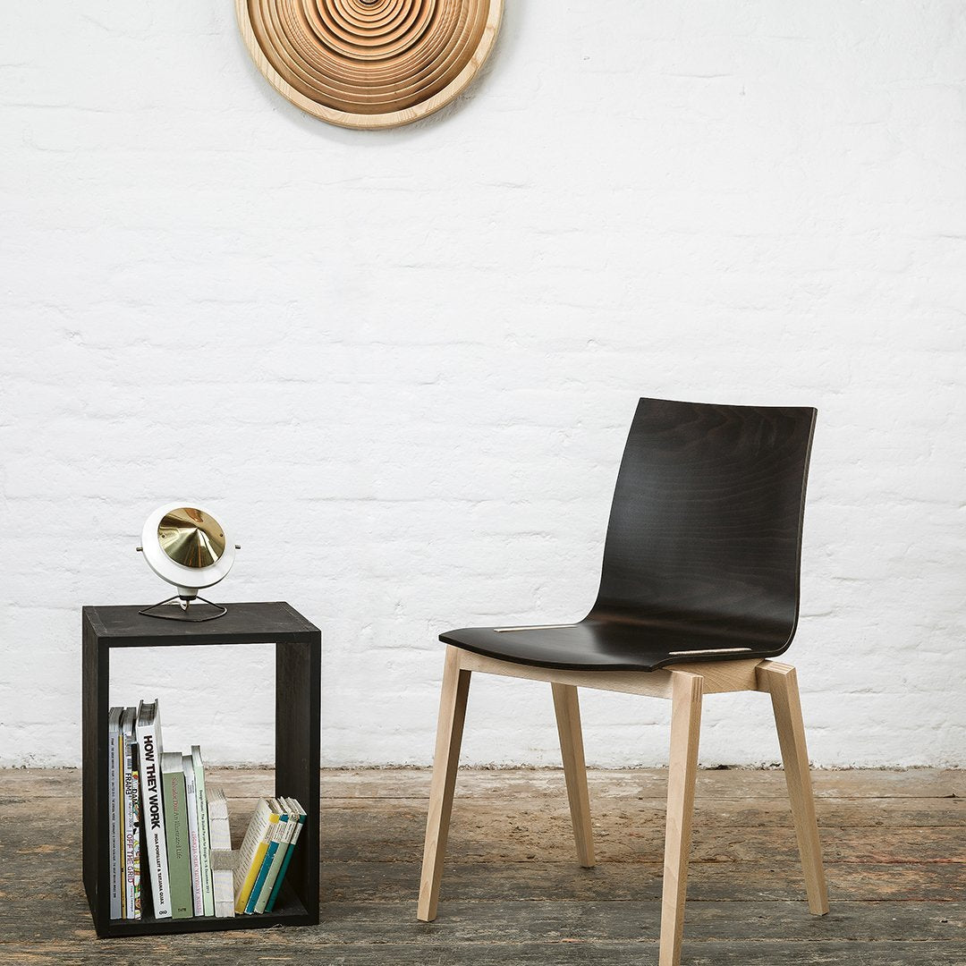 Sleek black chair with natural wood legs, set against a textured white wall and geometric wooden decor.