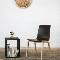 Sleek black chair with natural wood legs, set against a textured white wall and geometric wooden decor.