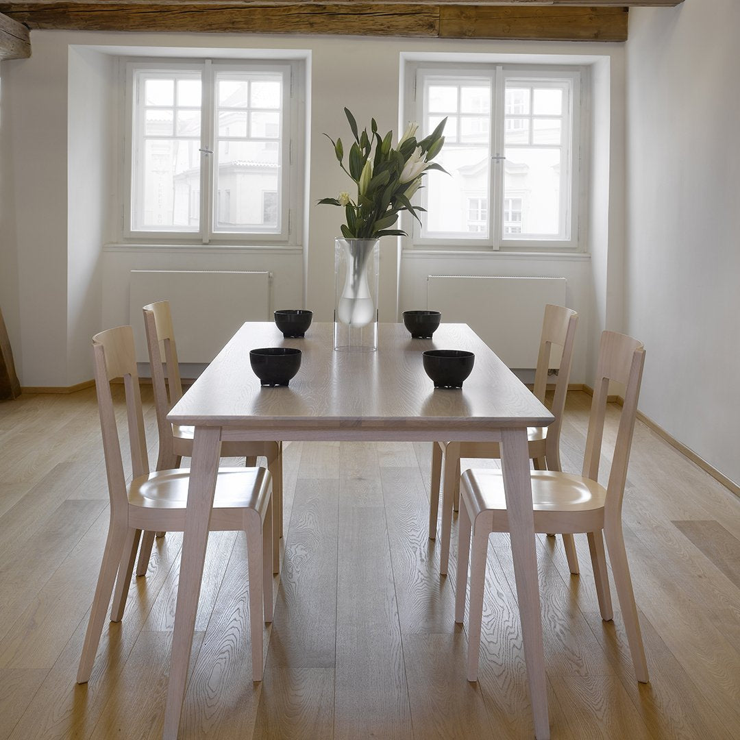 Light wood dining table with four white chairs and black ceramic bowls, set against a bright, minimalist interior.