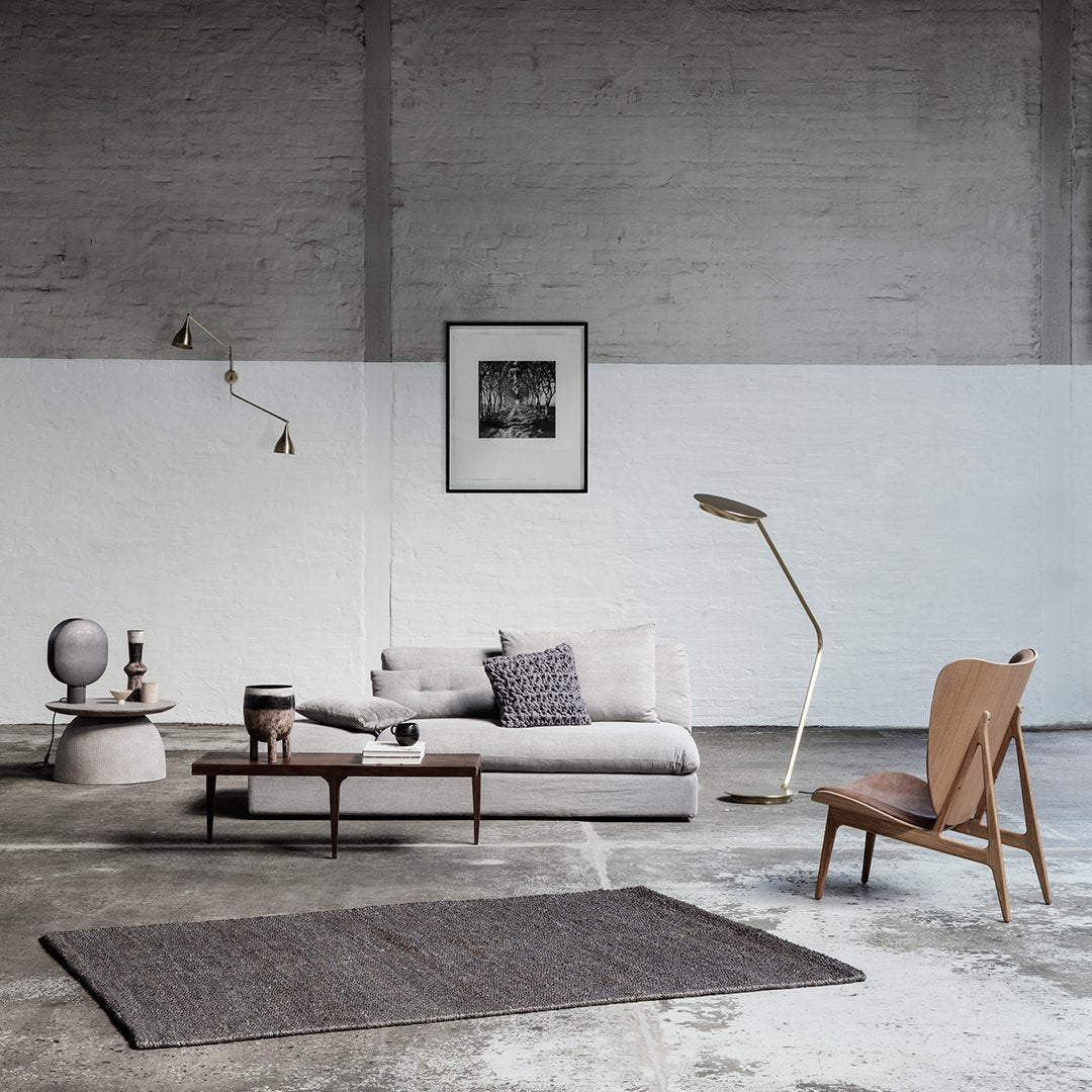 Cozy gray sofa with patterned cushions, light wood accents, and a dark woven rug in a minimalist room setting.