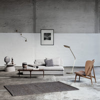 Cozy gray sofa with patterned cushions, light wood accents, and a dark woven rug in a minimalist room setting.