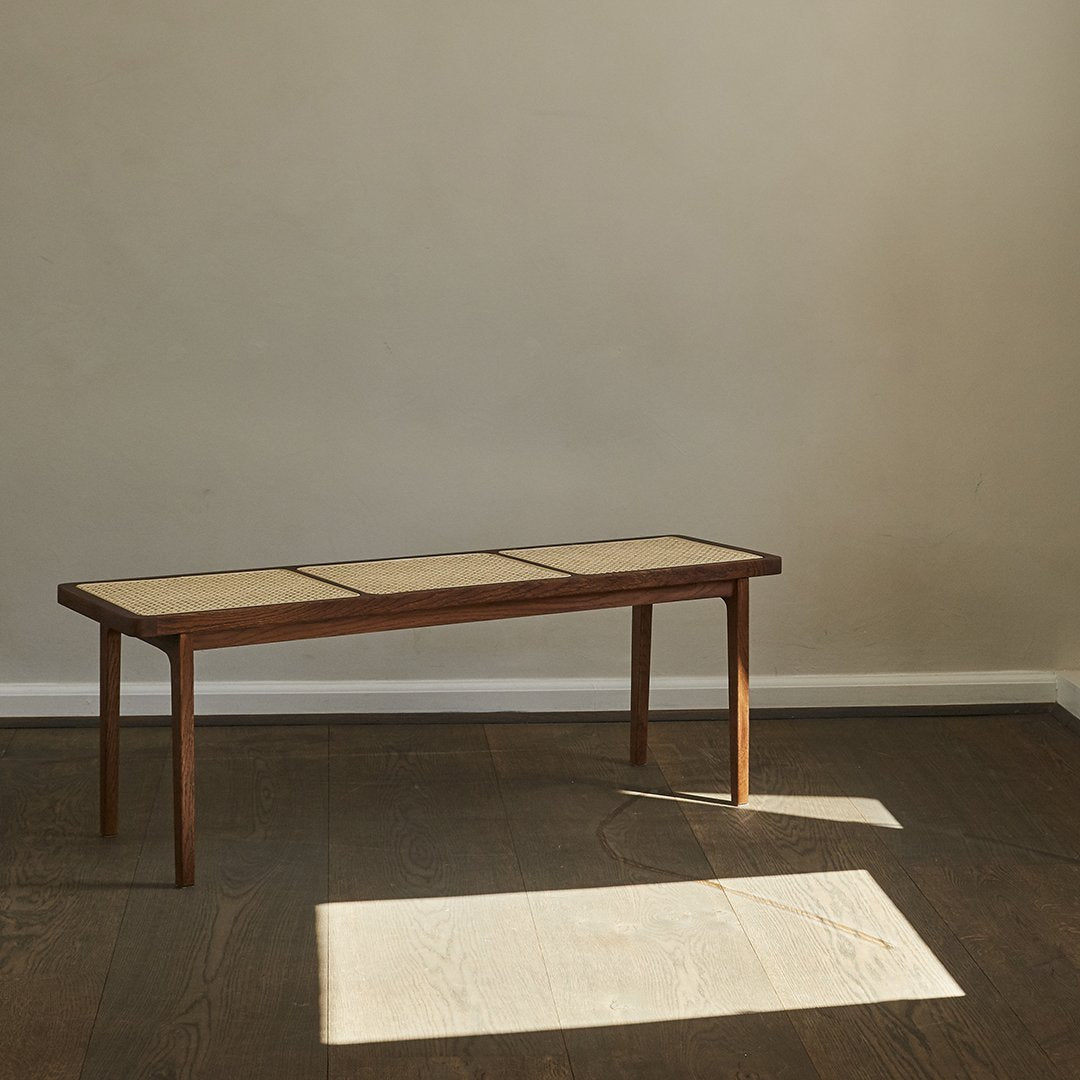Mid-century modern wooden bench featuring a light beige top and rich walnut legs, set against a muted wall.