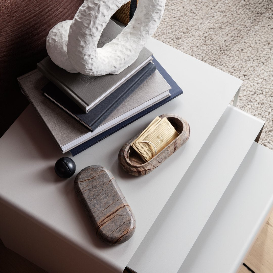 Gray and beige patterned storage boxes with smooth finishes on a modern white table. Textured decorative objects in background.