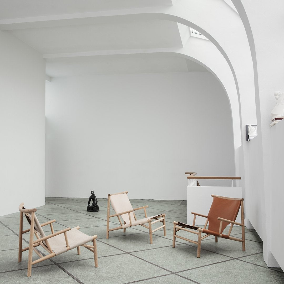 Modern chairs in neutral beige and brown tones, featuring sleek wooden frames and minimalist designs, on textured gray flooring.