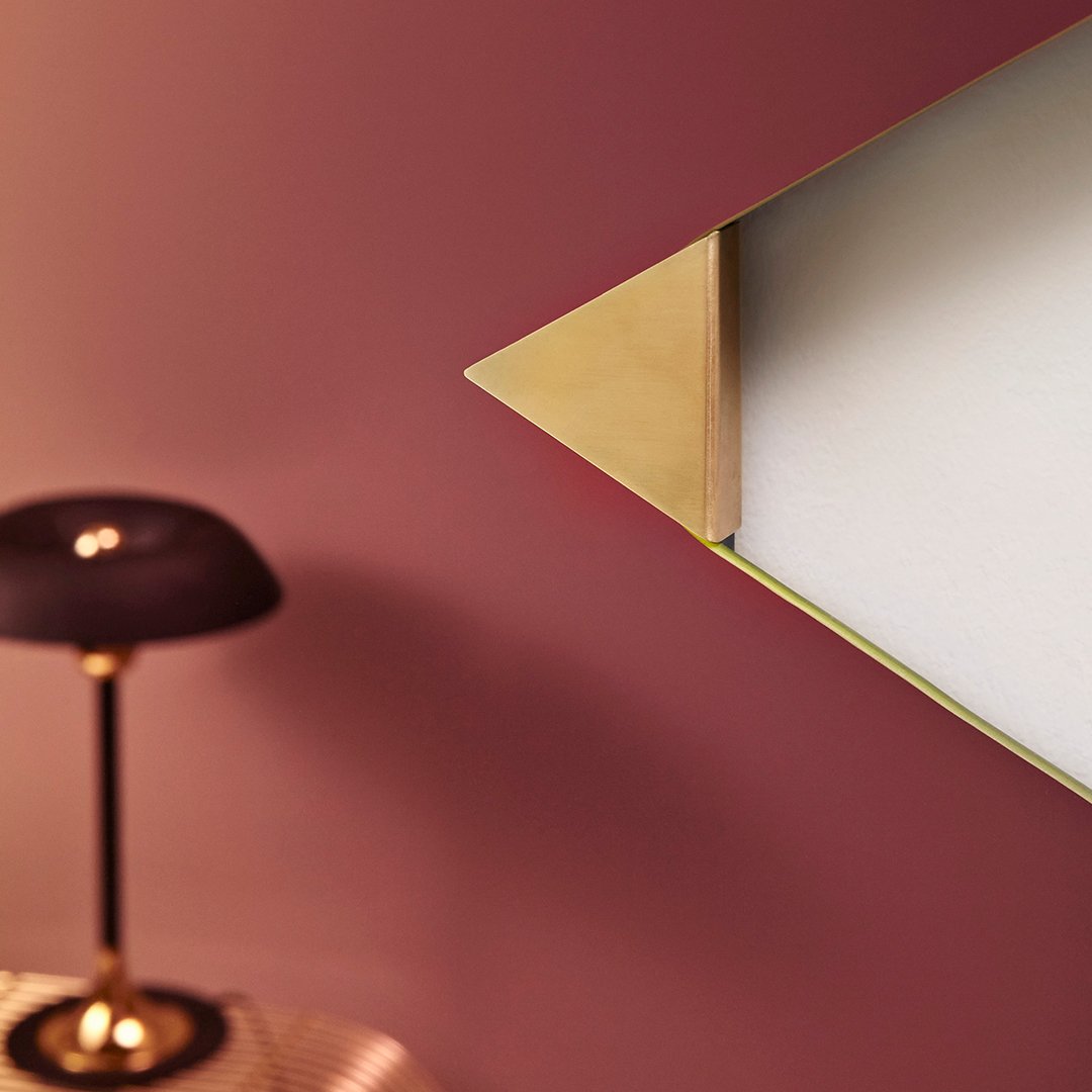 Geometric gold accent on white surface against a rich burgundy wall, paired with a sleek black lamp.