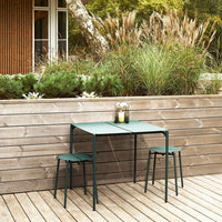 Green metal table and stools with a minimalist design, surrounded by natural greenery and wooden decking.