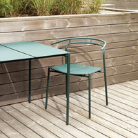 Green metal table and chair with a sleek modern design, set against a wooden backdrop and patio flooring.