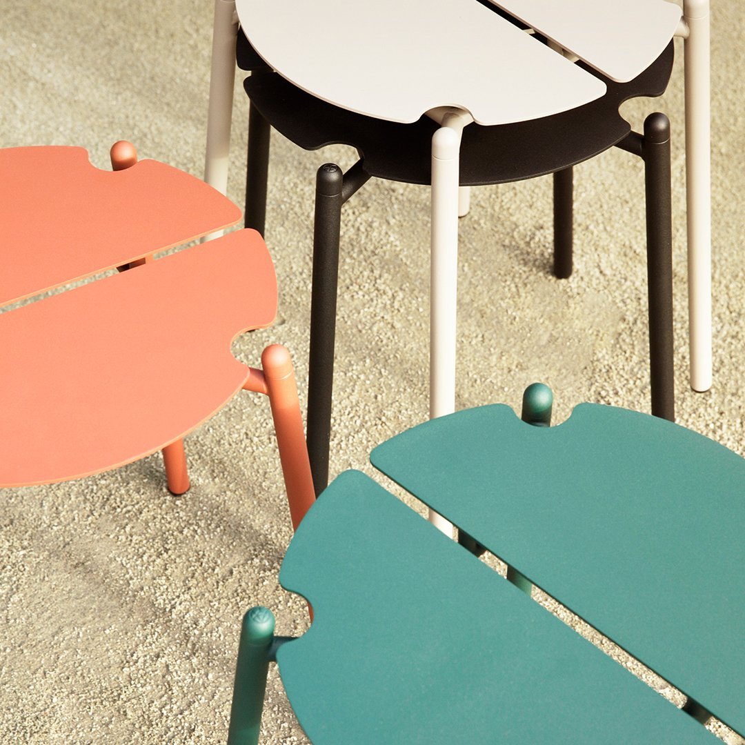 Colorful eclectic tables featuring coral, teal, black, and white finishes with playful leaf shapes.
