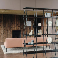 Modern black metal bookshelf with geometric design, contrasting with soft pink sofa and warm wood accents.