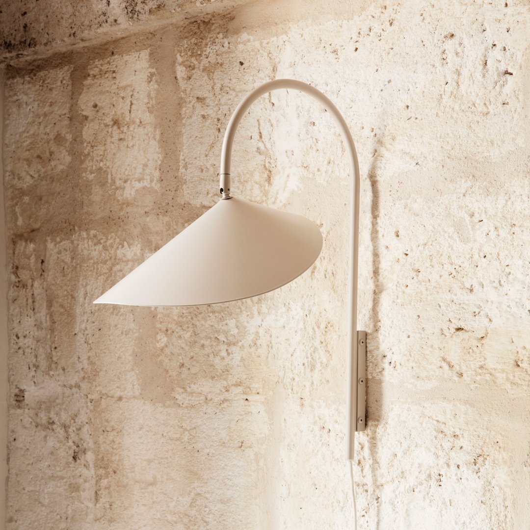 Modern white wall lamp with a sleek conical shade and minimalist silver arm against a textured beige stone wall.