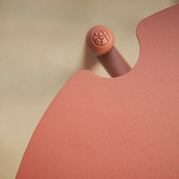 Rust-orange round table edge with a textured peach accent and soft curves against a neutral background.