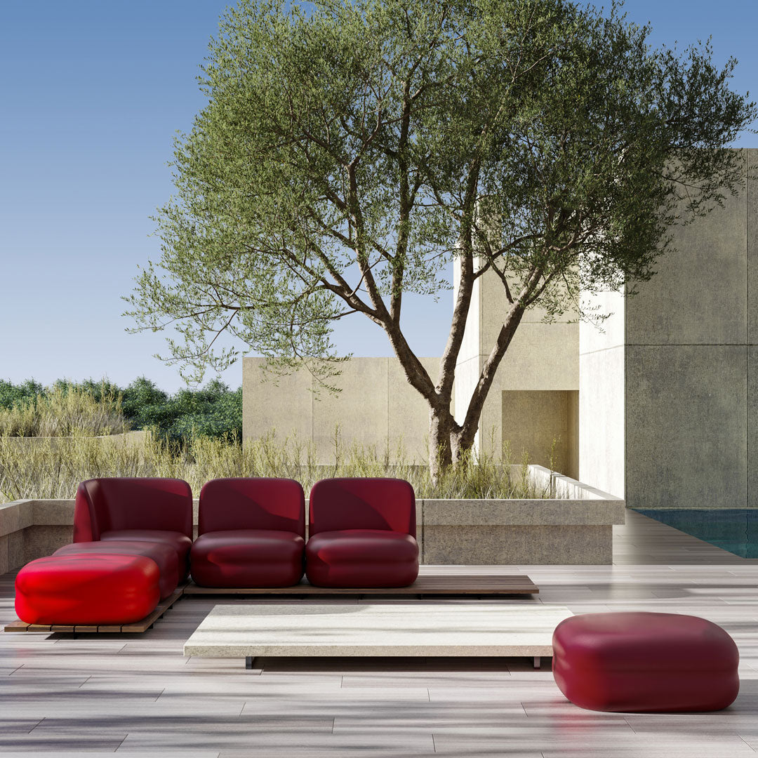 Modern red sectional sofa and ottoman, featuring sleek lines and a bold color against a neutral outdoor backdrop.