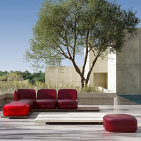 Modern red sectional sofa and ottoman, featuring sleek lines and a bold color against a neutral outdoor backdrop.