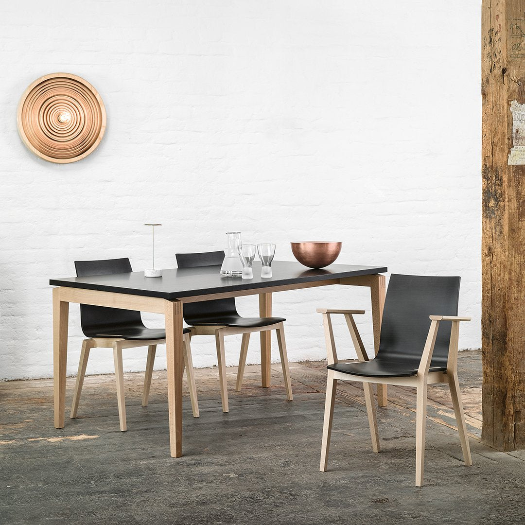 Black dining table with natural wood legs and matching black chairs, set against a white wall and rustic wood accents.