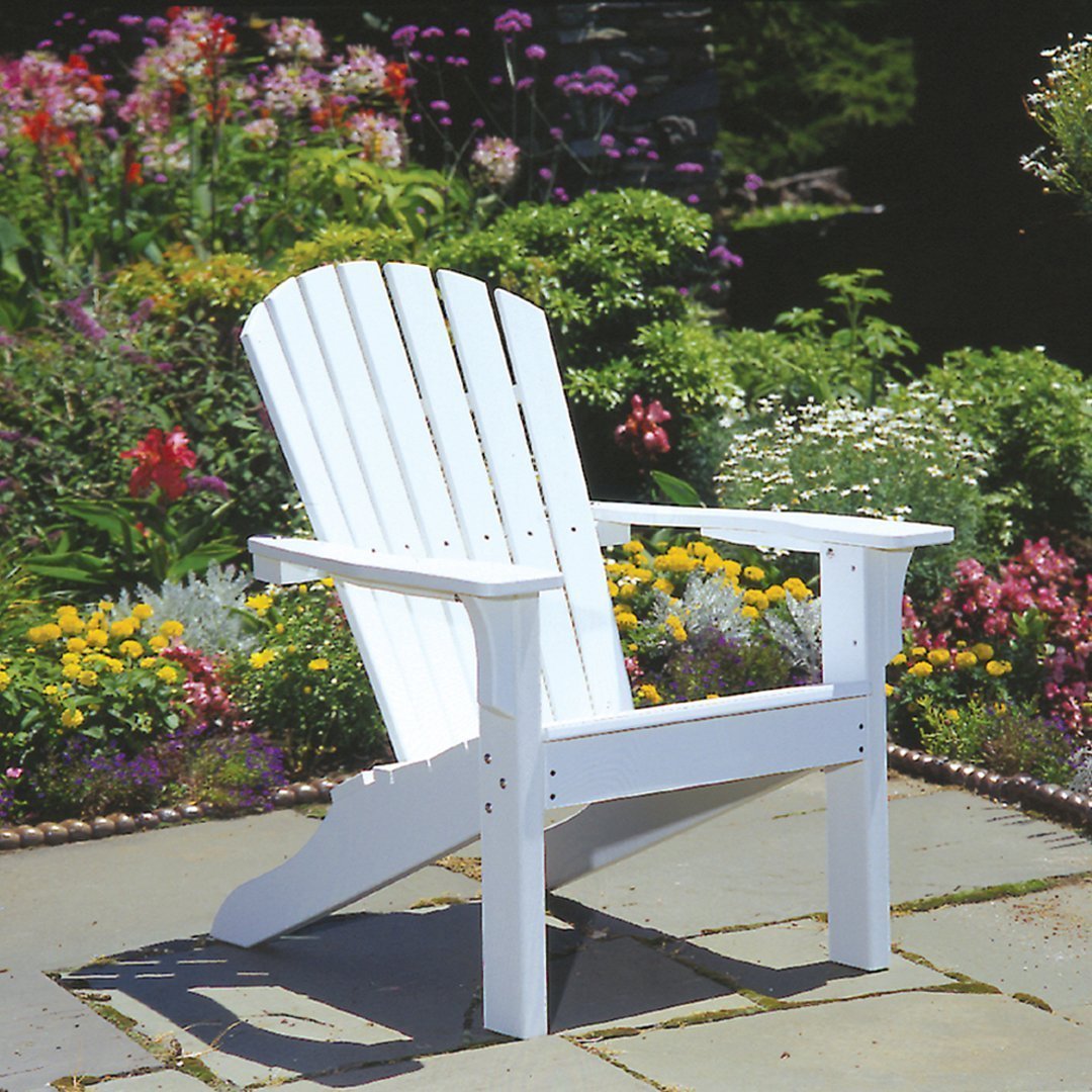 White adirondack chair on a stone patio, surrounded by colorful blooming flowers and lush greenery.