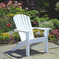 White adirondack chair on a stone patio, surrounded by colorful blooming flowers and lush greenery.