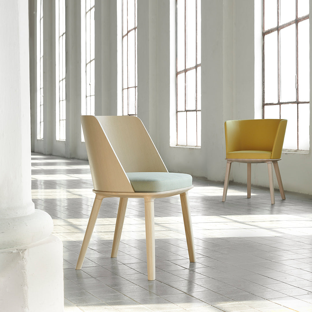 Light beige and soft mint chair with wooden legs; bright yellow accent chair in a spacious, airy setting.