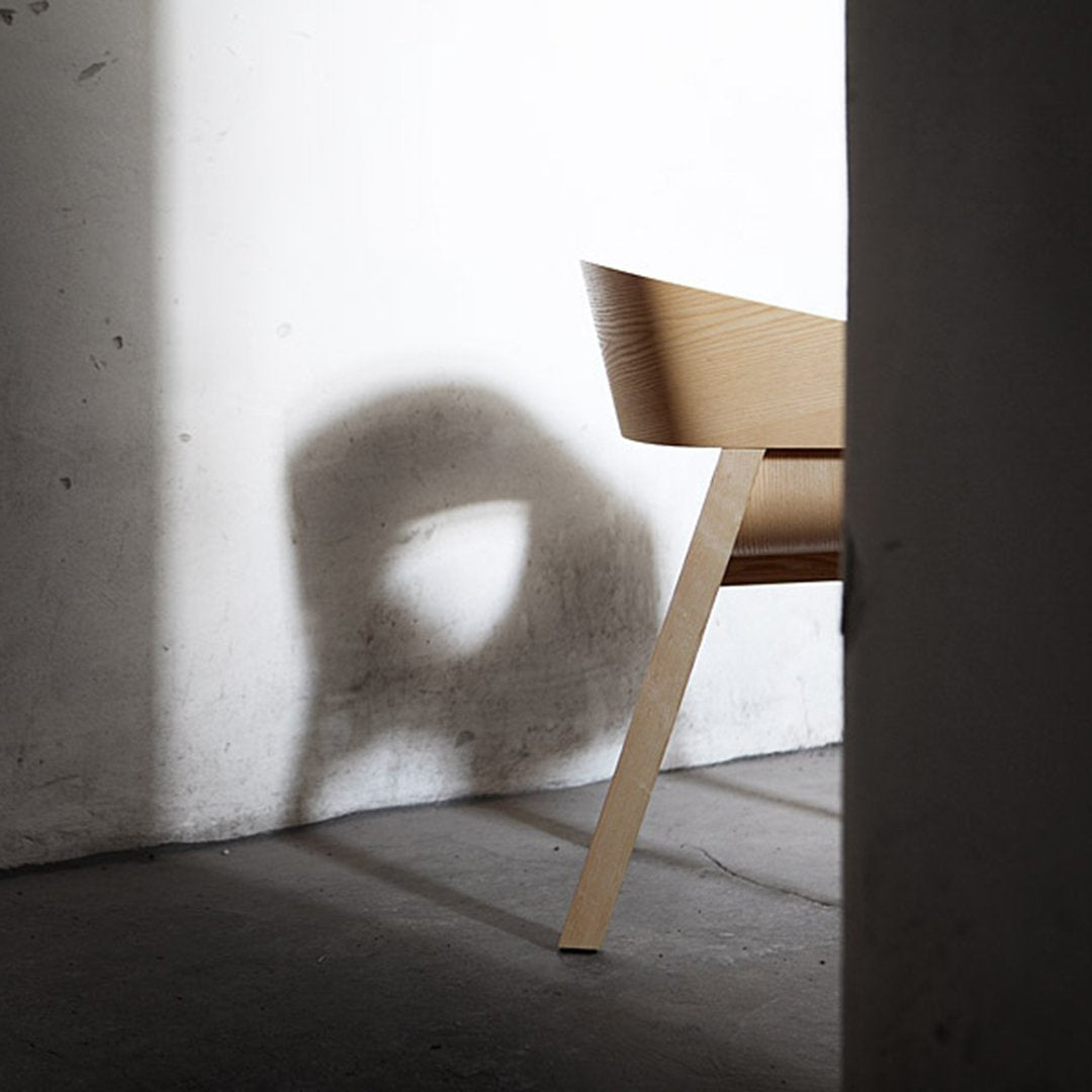 Wooden chair casting shadow on a textured wall, showcasing natural wood tones and minimalist design.