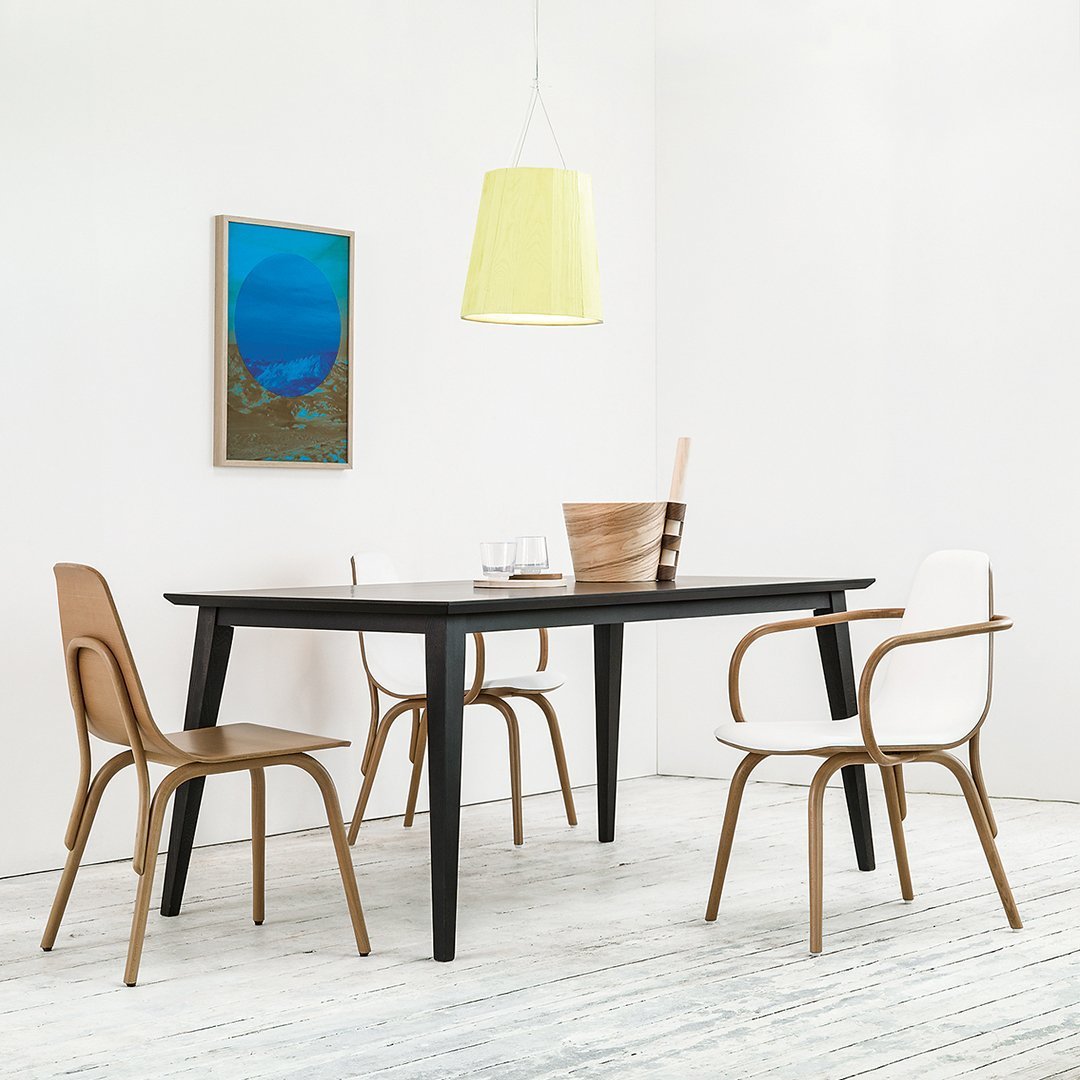 Modern black dining table surrounded by beige and white chairs, accented by a bright yellow pendant light.