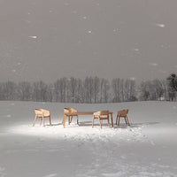 Light wood dining table and chairs set against a snowy landscape with gray skies, creating a serene winter ambiance.