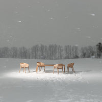 Light wood dining table and chairs set against a snowy, gray winter landscape, minimalistic design with natural textures.