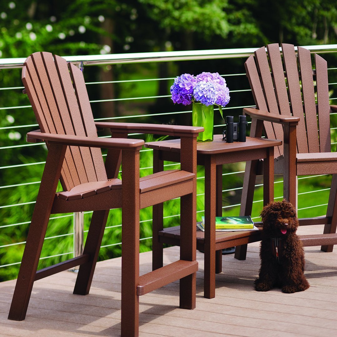 "Brown Adirondack chairs with vertical slats and a matching side table, complemented by purple flowers and green foliage."