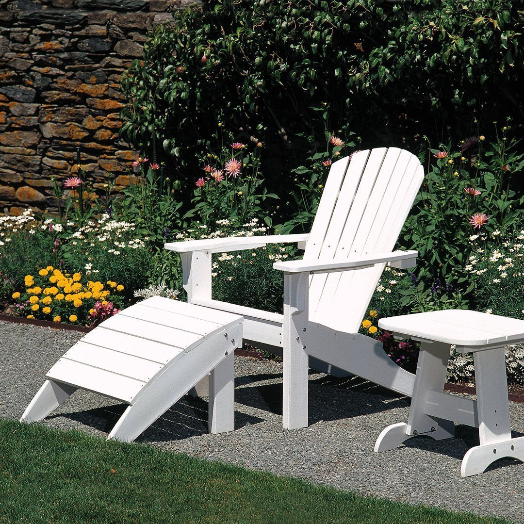 White Adirondack chair and matching side table in a garden setting, surrounded by vibrant flowers and greenery.