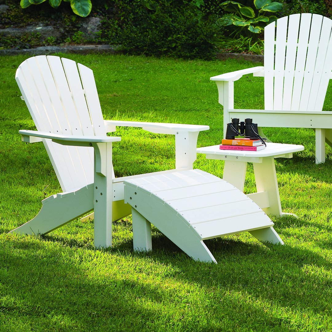 White Adirondack chairs with a matching footrest, set on green grass, creating a serene outdoor seating space.