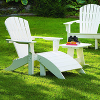 White Adirondack chairs with a matching footrest, set on green grass, creating a serene outdoor seating space.
